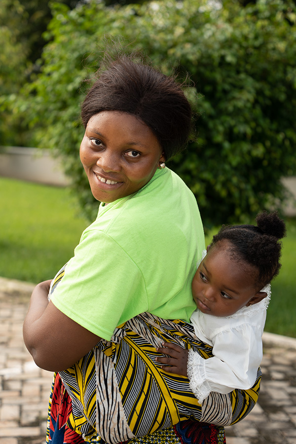 Smiling woman in green shirt with child strapped to back.