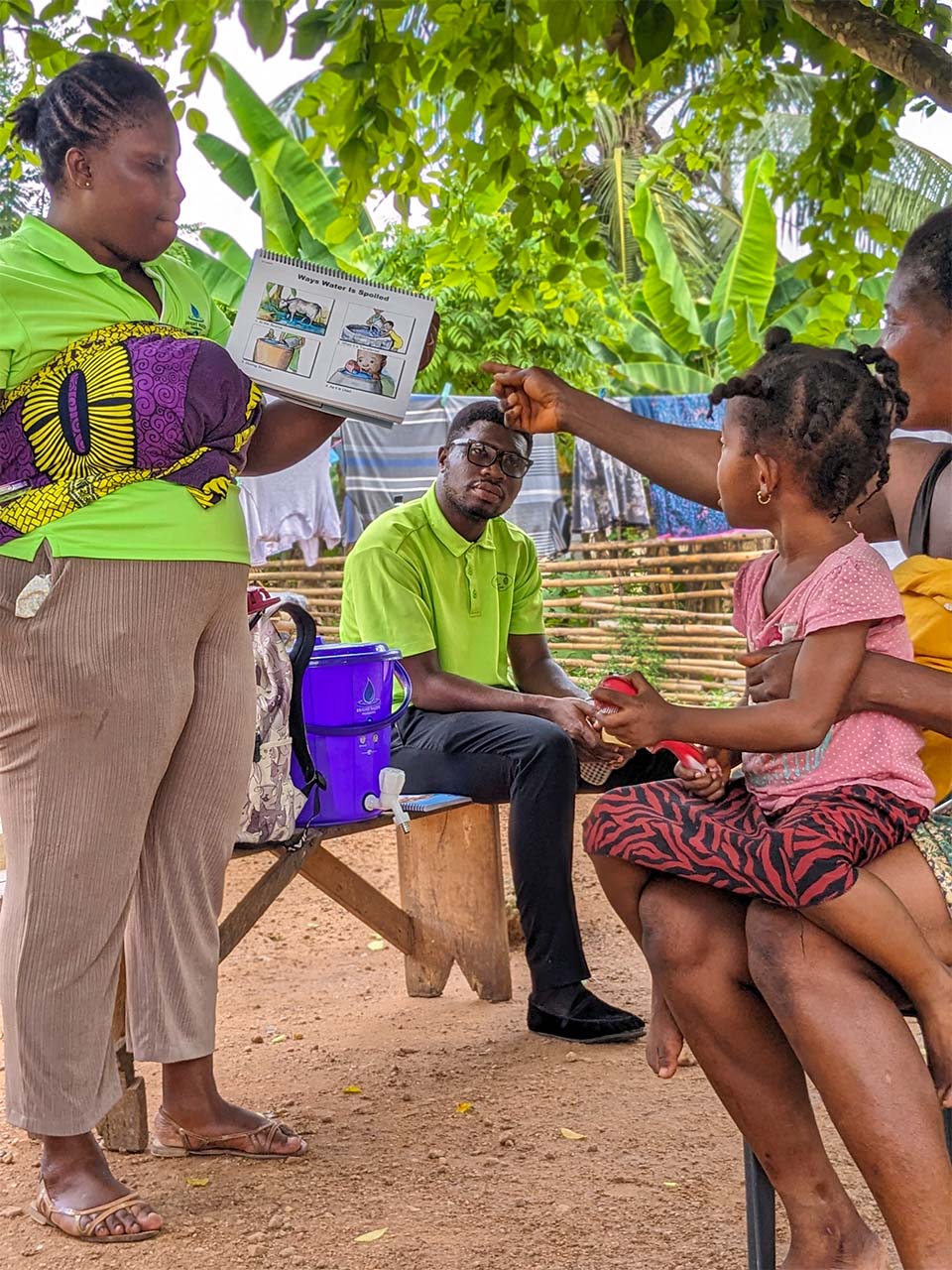 Woman in green shirt teaches mother and child about safe frinking water.