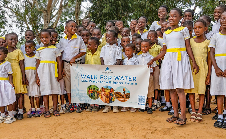 Ghanaian school kids dressed in white and yellow standing with Walk for Water banner.