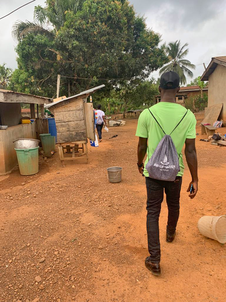 Many in green shirt walks away down a road. His backpack reads Bright Water.